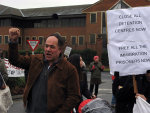 People gather in front of the main entrance with placards and vocal resistance