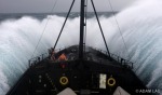 Crew bracing as ship plunges into the trough of massive waves in rough seas