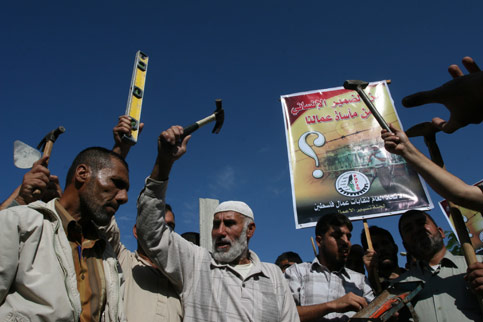 Palestinian workers, holding work tools, chant slogans as they demonstrate again