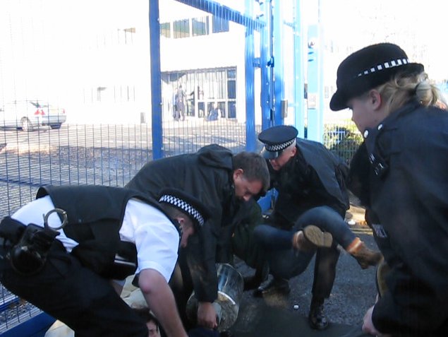 Police officers lift and move activists and concrete lock on.